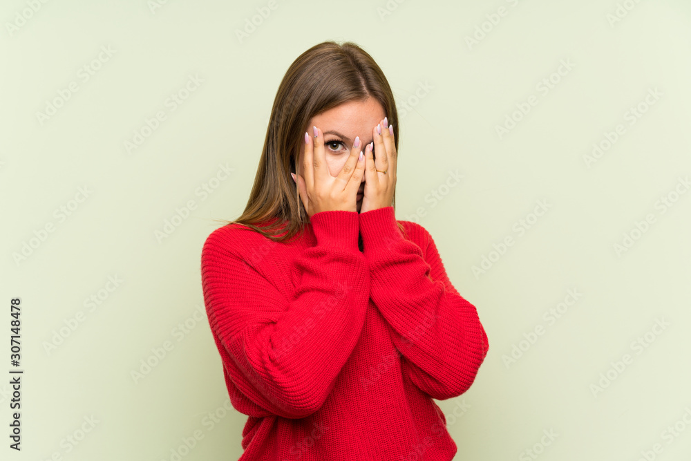 Teenager girl over isolated green background covering eyes and looking through fingers Teenager girl over isolated green background covering eyes and looking through fingers