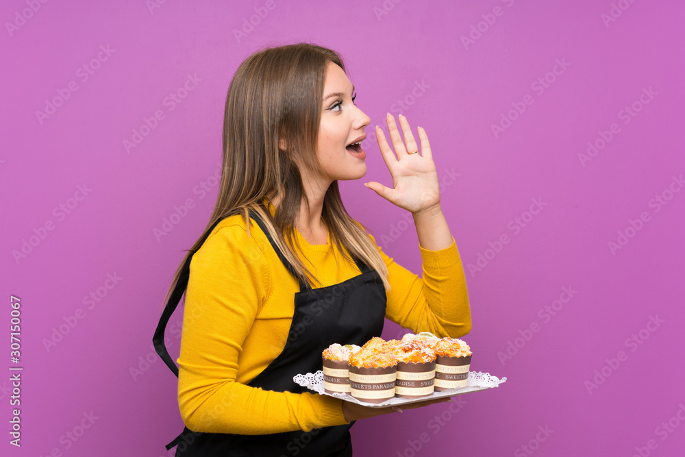 Teenager girl holding lots of different mini cakes over isolated purple background shouting with mouth wide open Teenager girl holding lots of different mini cakes over isolated purple background shouting with mouth wide open