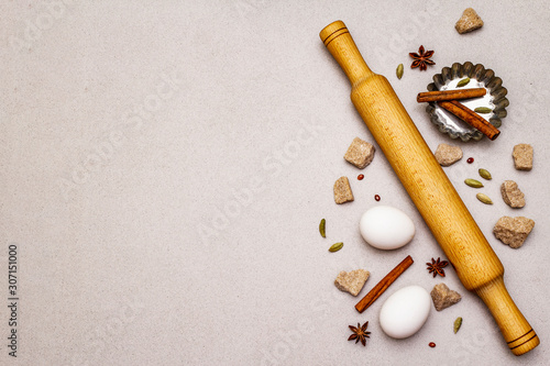 Christmas cooking background, spices, eggs, brown lump sugar, cupcake baking dish and a rolling pin. Light stone concrete background