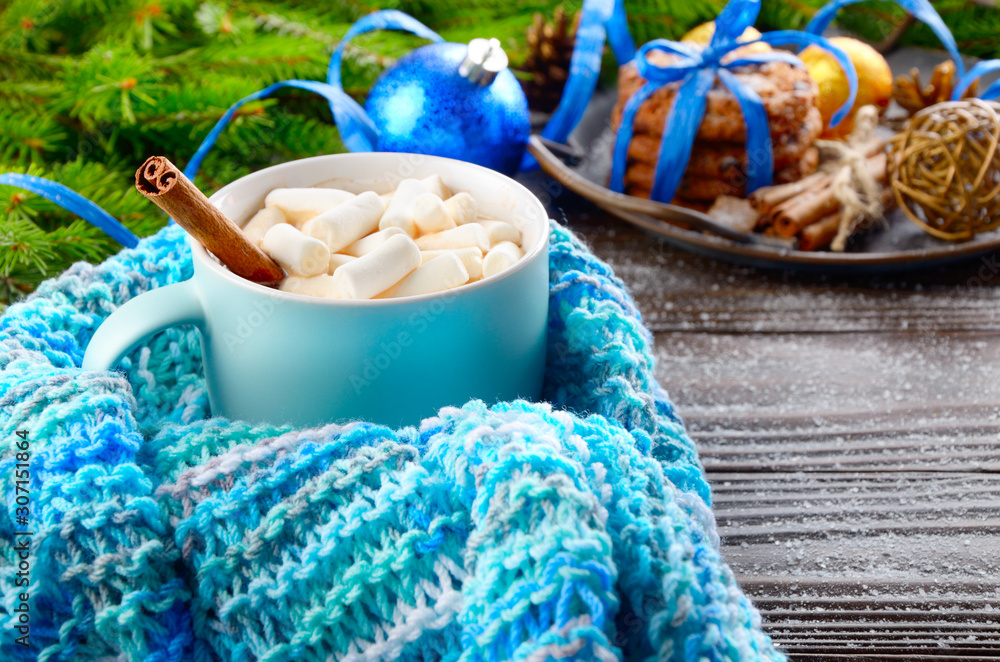 Christmas background of blue hot chocolate mug with marshmallows in knitted scarf, spruce branch and tray with gingerbread cookies on wooden table Christmas background of blue hot chocolate mug with marshmallows in knitted scarf, spruce branch and tray with gingerbread cookies on wooden table