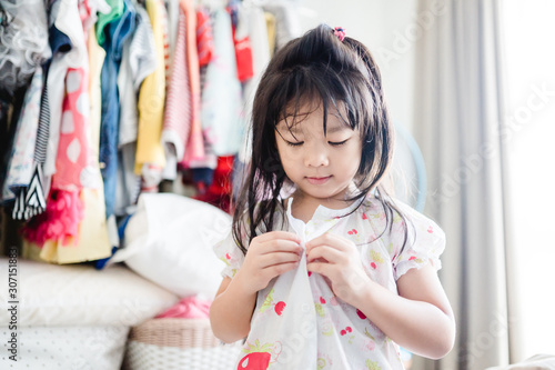 Little asian girl trying to button a pajamas by herself.Kindergarten school girl wake up and ready for shower in the morning for go to school child development by learning to do things by themselves.