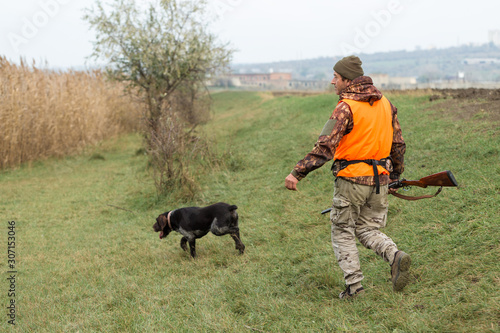 Hunting period, autumn season open. A hunter with a gun in his hands in hunting clothes in the autumn forest in search of a trophy. A man stands with weapons and hunting dogs tracking down the game. © Mountains Hunter
