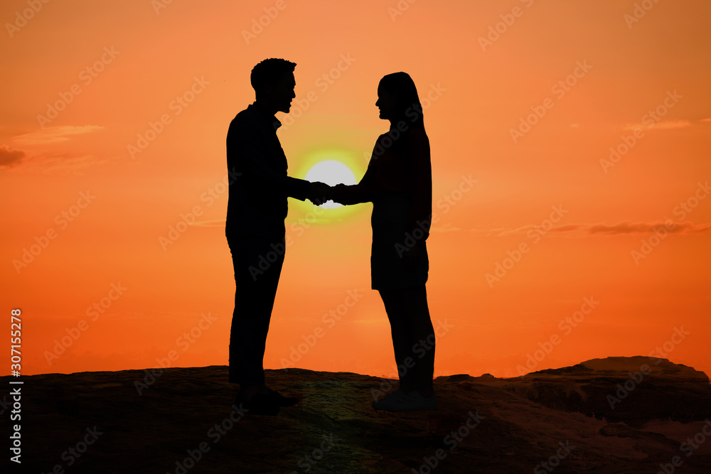Silhouette of man and woman holding hands together at big sunset and romantic background