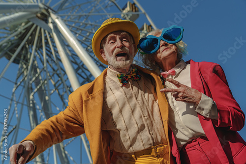 Joyful old couple in ridiculous clothes near attraction