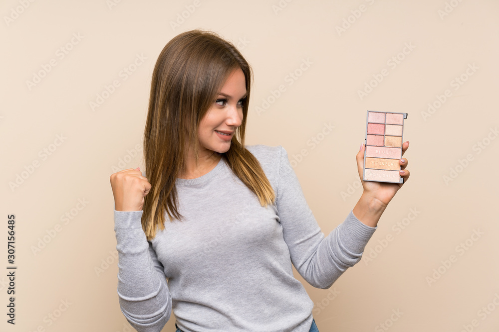 Teenager girl with makeup palette over isolated background celebrating a victory Teenager girl with makeup palette over isolated background celebrating a victory