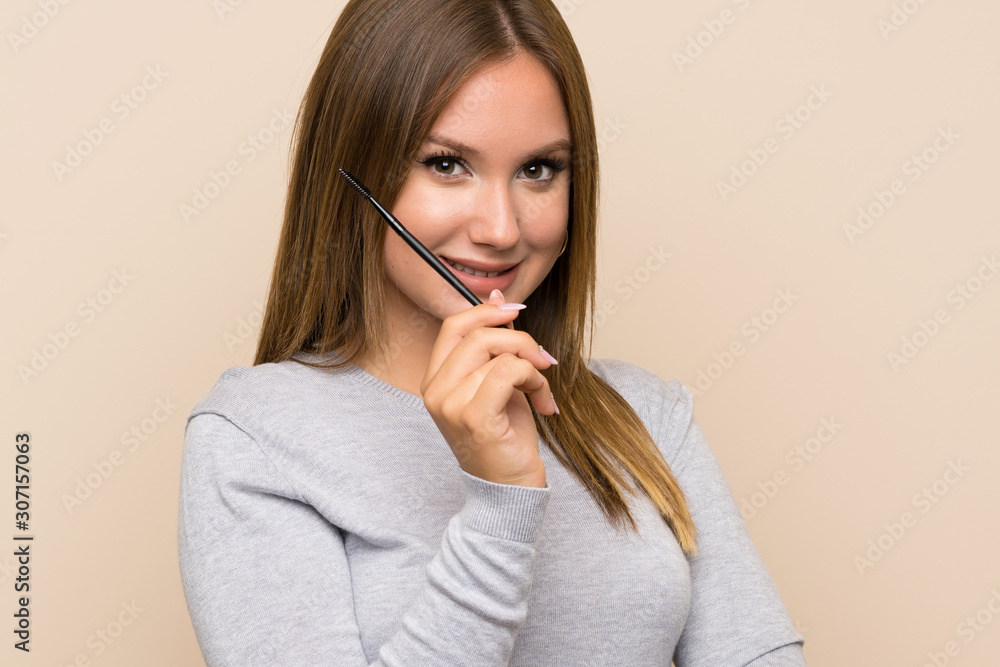 Teenager girl applying mascara with cosmetic rush over isolated background Teenager girl applying mascara with cosmetic rush over isolated background