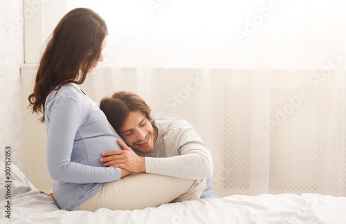 Handsome happy man listening wife's pregnant belly