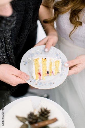 Winter wedding outdoors in forest, the newlyweds cut the wedding cake. Cropped image of hands of bride and groom holding white plate with piece of wedding cake
