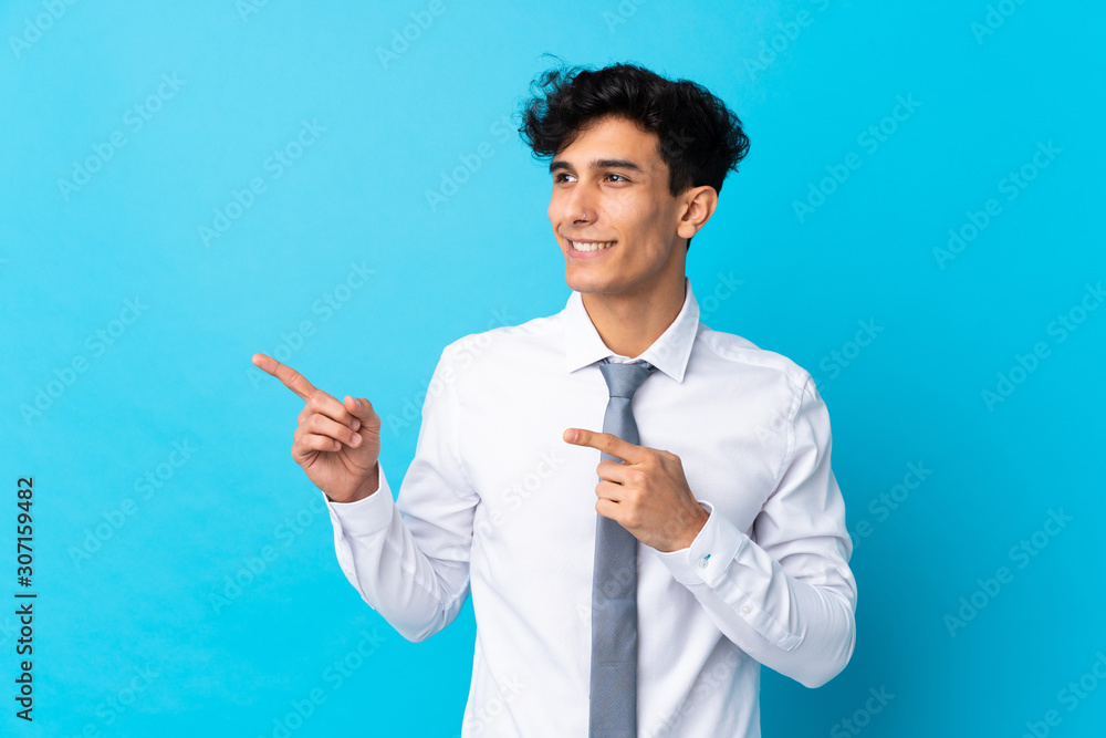 Young Argentinian businessman over isolated blue background pointing finger to the side Young Argentinian businessman over isolated blue background pointing finger to the side
