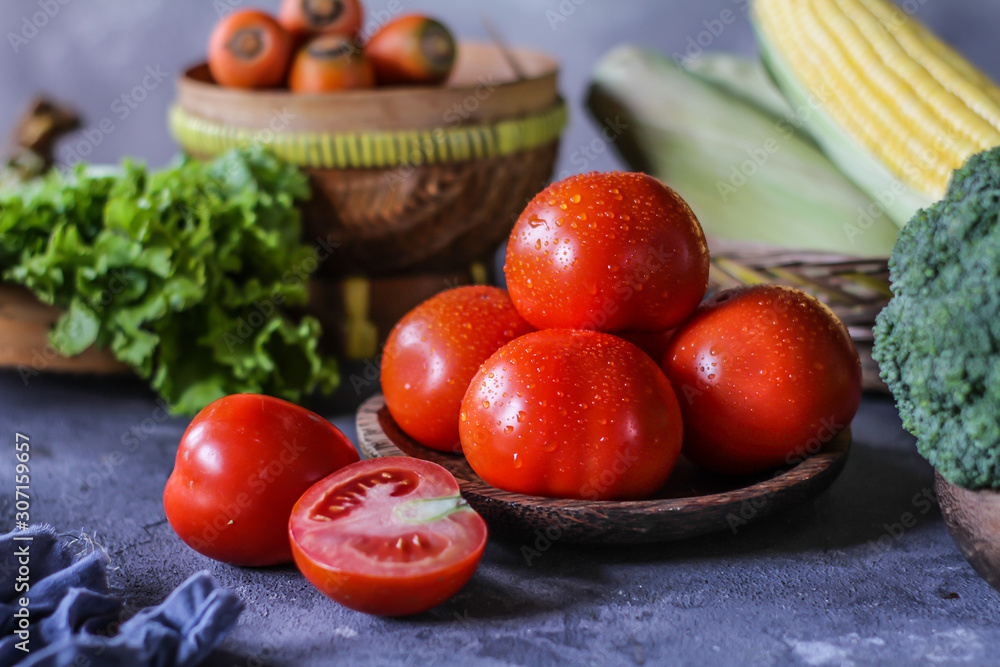 Photo of fresh tomatoes in a bowl on dark background around vegetables, carrot, salt, black pepper, corn, broccoli. Slice tomatoes. Harvesting tomatoes. Drops of water vegetables. Wooden table. Image Photo of fresh tomatoes in a bowl on dark background around vegetables, carrot, salt, black pepper, corn, broccoli. Slice tomatoes. Harvesting tomatoes. Drops of water vegetables. Wooden table. Image