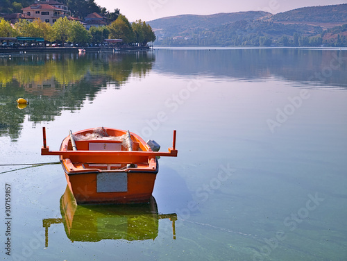 Lake Orestiada, Kastoria, Greece,  boat and reflection on calm water. Trees and mountains mirroring on water surface.