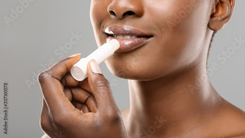 Unrecognizable afro girl applying hygienic lip balm over gray background