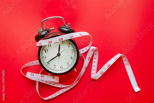 Black alarm clock and measuring tape on red background.Time to diet concept