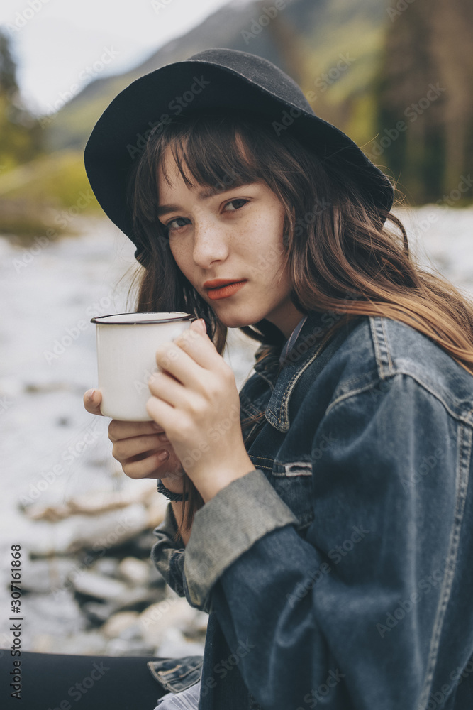 Girl wearing backpack drinking tea from thermos and looking at the Girl wearing backpack drinking tea from thermos and looking at the