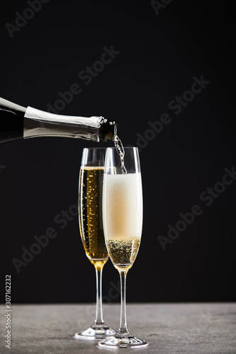 sparkling wine pouring from bottle into glasses for celebrating christmas on black