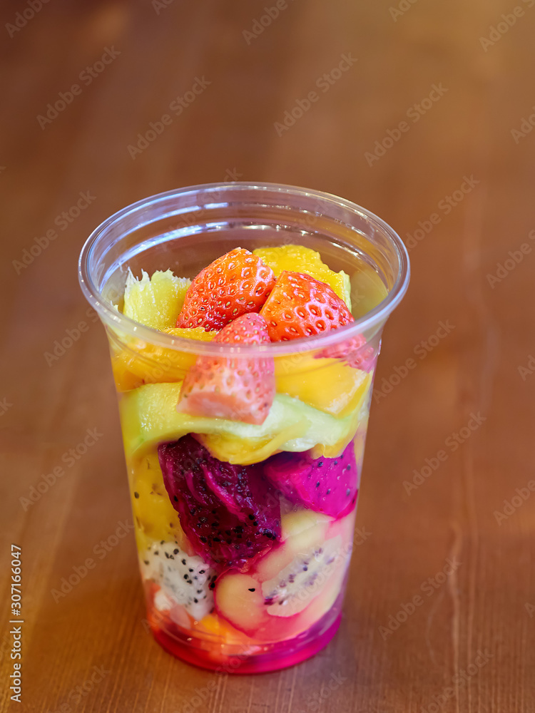 salad with mango, kiwi, strawberry, pineapple, pitaya, cactus fruit in a clear plastic Cup which is on a wooden table. health food. organic food. exotic fruit. close up. salad with mango, kiwi, strawberry, pineapple, pitaya, cactus fruit in a clear plastic Cup which is on a wooden table. health food. organic food. exotic fruit. close up.