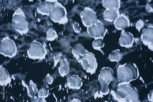 Ice surface of the reservoir. Abstract pattern consisting of a dark surface of thin ice and white spots of ice crystals. The view from the top. photo