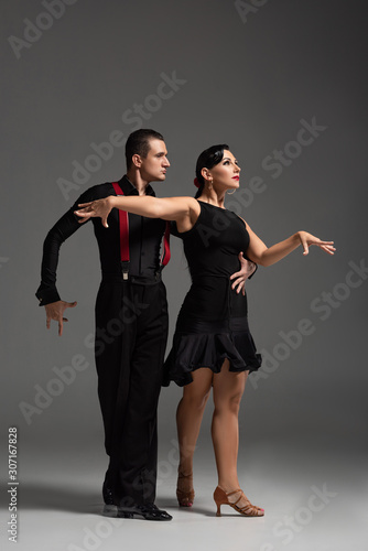elegant couple of dancers in black clothing performing tango on grey background