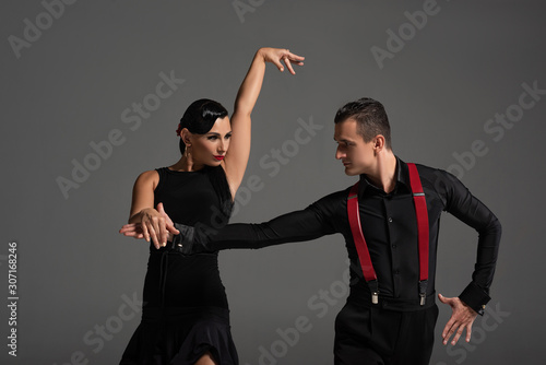 elegant couple of dancers looking at each other while performing tango isolated on grey