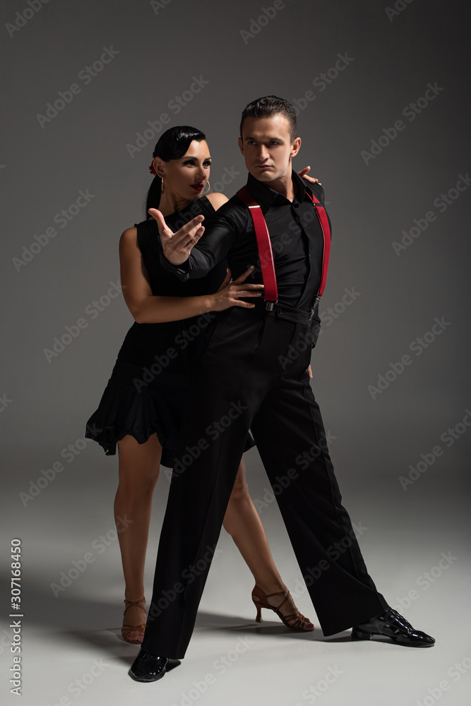 passionate couple of dancers in black clothing performing tango on grey background passionate couple of dancers in black clothing performing tango on grey background