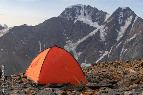 The tent is in the background of the steep cliffs in the snow. A beautiful dawn. Bright orange tent.