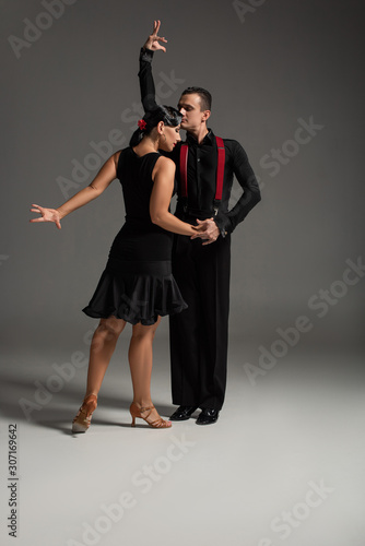 two expressive dancers in black clothing performing tango on grey background