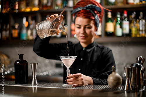 Bartender girl pouring a alcoholic drink from the measuring cup to a cocktail glass