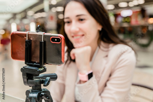 A young woman blogger in a mall works communicates on a mobile phone. Mobile phone on a tripod