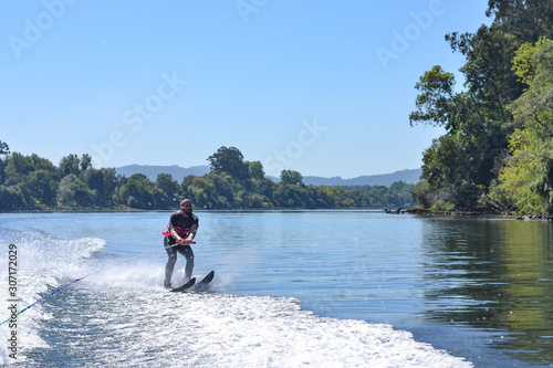 Young man water skiing over the river in summer, having fun photo