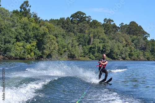 Young man water skiing over the river in summer, having fun