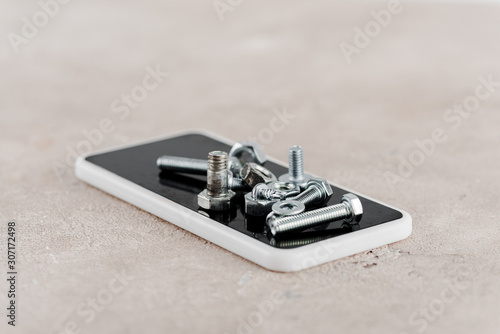 metal screws and bolts on smartphone on grey background