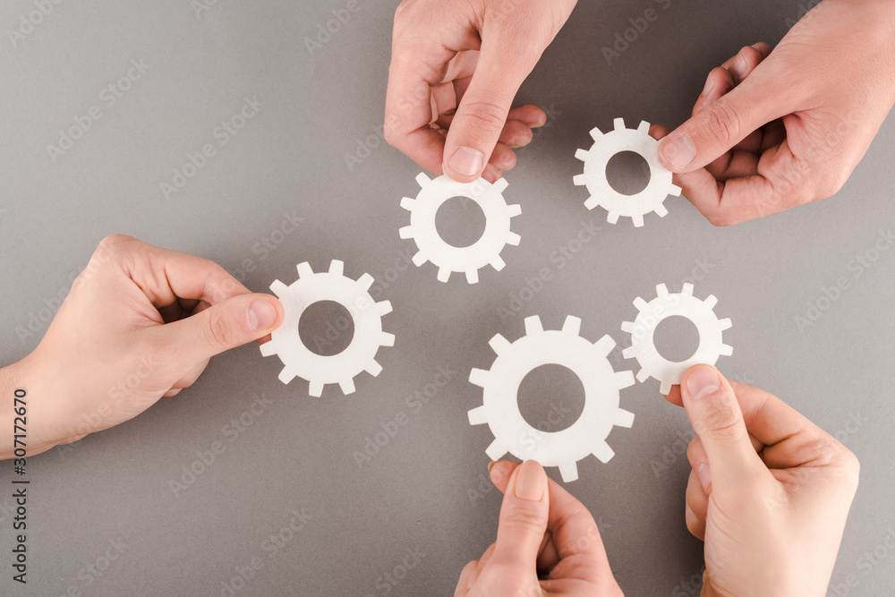 cropped view of people holding white gears on grey background cropped view of people holding white gears on grey background