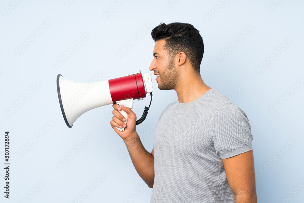 Young handsome man over isolated background shouting through a megaphone Young handsome man over isolated background shouting through a megaphone