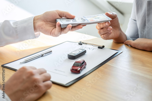 Car rental and Insurance concept  Young salesman receiving money and giving car s key to customer after sign agreement contract with approved good deal for rent or purchase