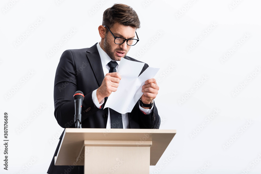 scared businessman in suit standing at podium tribune and rearing paper during conference isolated on white