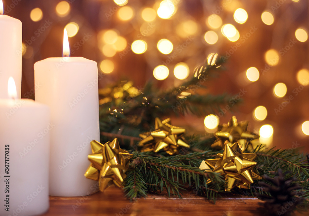 Golden Christmas ball on a tree branch, white candle flame with stars bokeh lights on a brown background