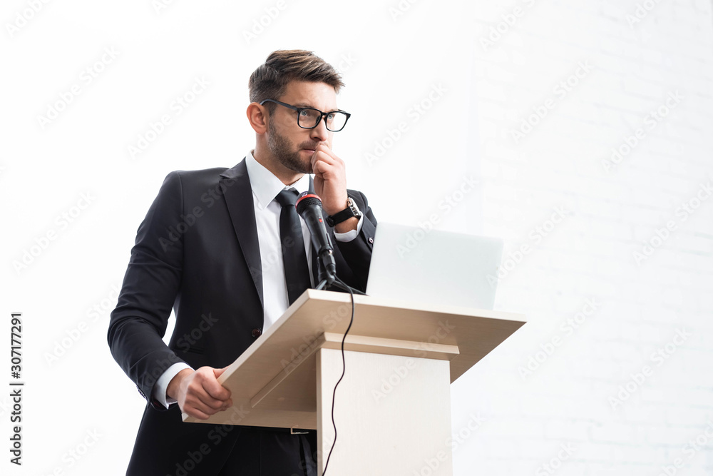low angle view of scared businessman in suit standing at podium tribune during conference isolated on white low angle view of scared businessman in suit standing at podium tribune during conference isolated on white