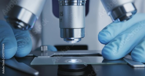 Close-up shot of sample slide and microscope with metal lens at laboratory.
