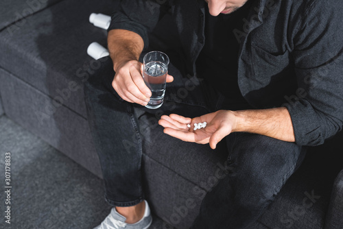 Quadro su tela cropped view of man with panic attack holding pills and glass of water in apartm