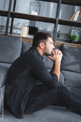 side view of handsome man with panic attack sitting on floor in apartment