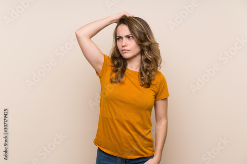 Young blonde girl over isolated background having doubts while scratching head