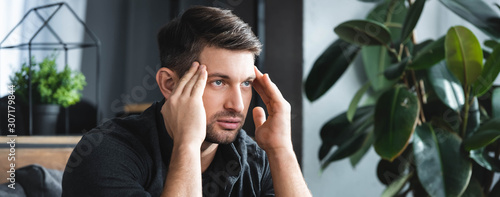 Foto panoramic shot of handsome man with headache touching head in apartment