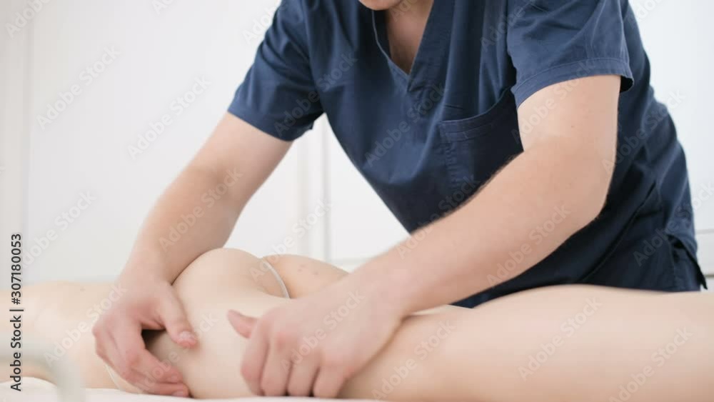 Close-up of a male physiotherapist doing a light massage to warm up the hips and buttocks of a young woman in a professional spa salon next to a sprig of cotton. 4K massage body care concept Close-up of a male physiotherapist doing a light massage to warm up the hips and buttocks of a young woman in a professional spa salon next to a sprig of cotton. 4K massage body care concept