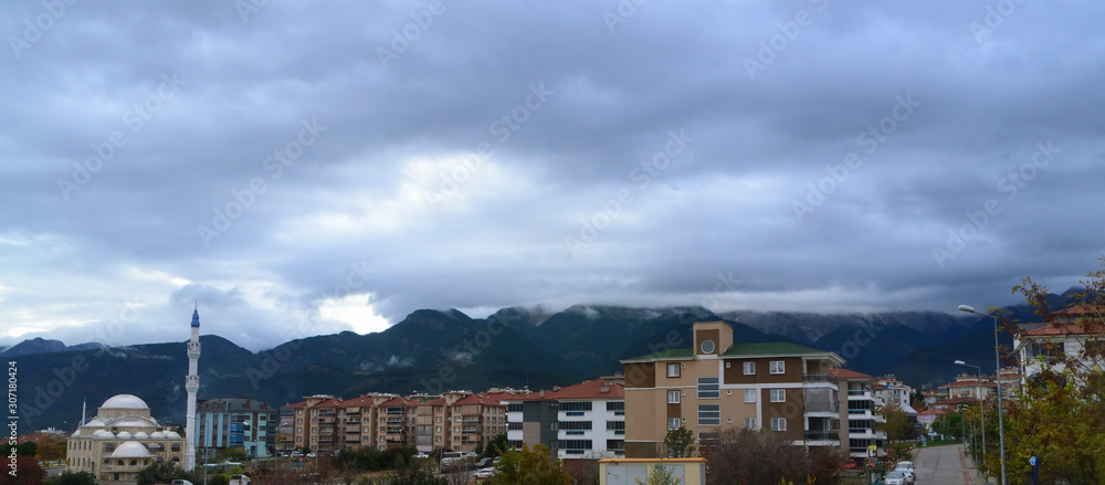 A mountain covered with clouds captured with buildings, mosque and trees on background.