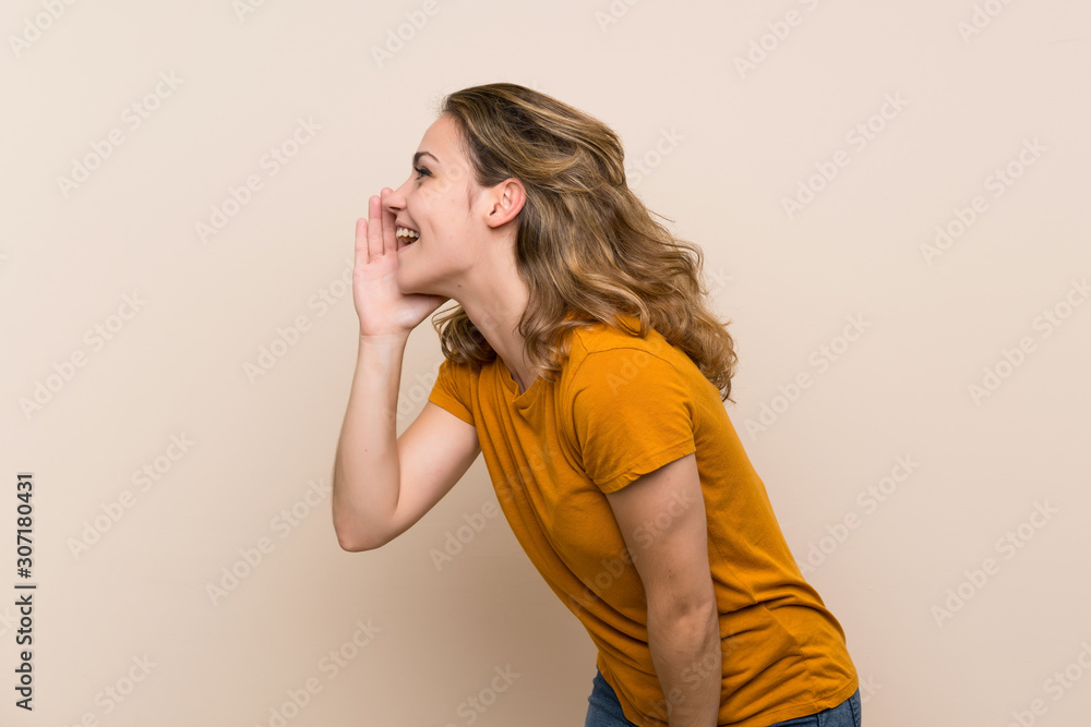 Young blonde girl over isolated background shouting with mouth wide open to the lateral Young blonde girl over isolated background shouting with mouth wide open to the lateral