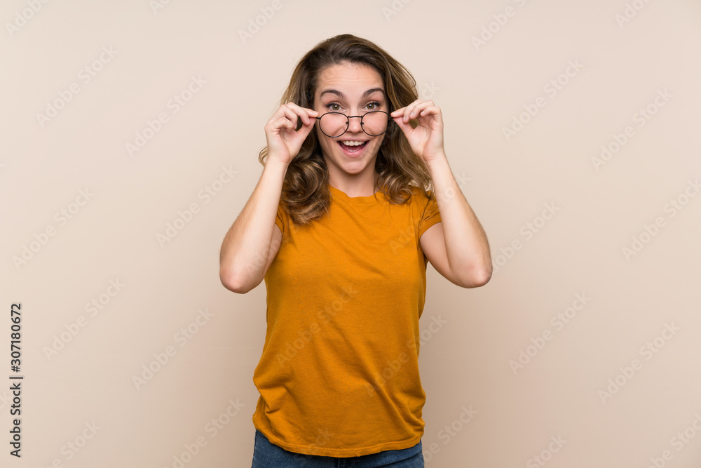 Young blonde girl over isolated background with glasses and surprised Young blonde girl over isolated background with glasses and surprised