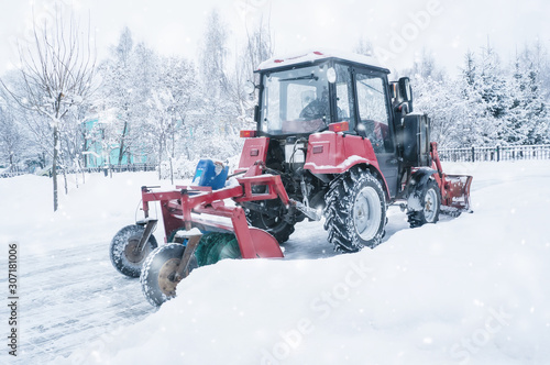 A red old tractor clears the street of snow in a snow storm. Street cleaning in winter