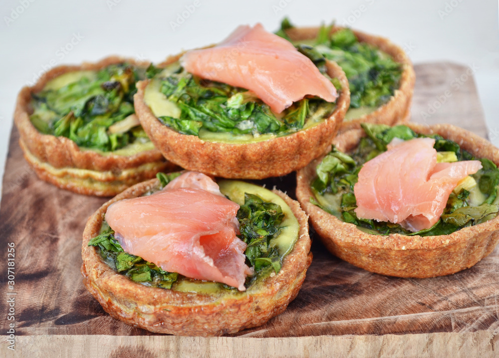 Rye flour quiche with spinach, eggs and lightly salted salmon. Delicious  appetizer on wooden cut board. 