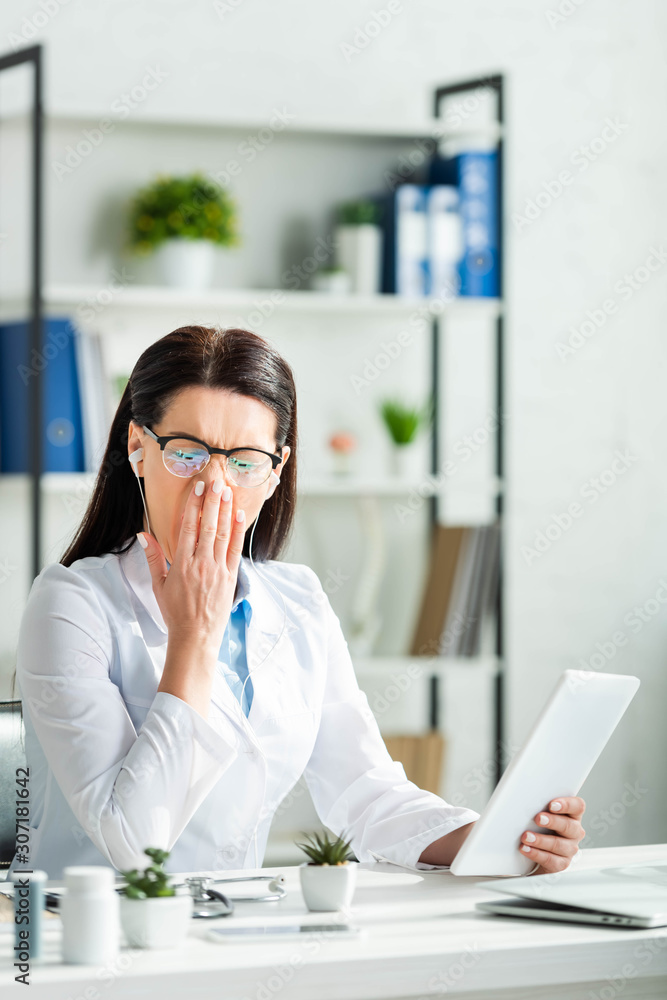 tired doctor yawning and having online consultation on digital tablet in clinic office tired doctor yawning and having online consultation on digital tablet in clinic office
