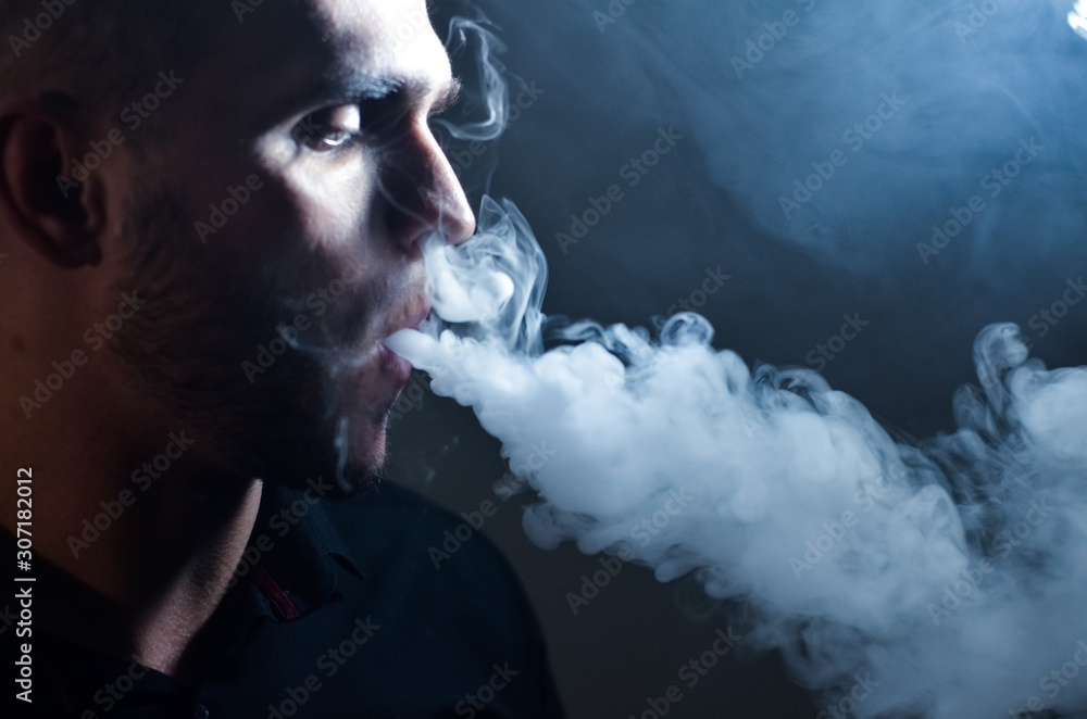 Man vaping e-cigarette with e-liquid, close-up, breathes out large cloud of steam or vapor. Vape concept